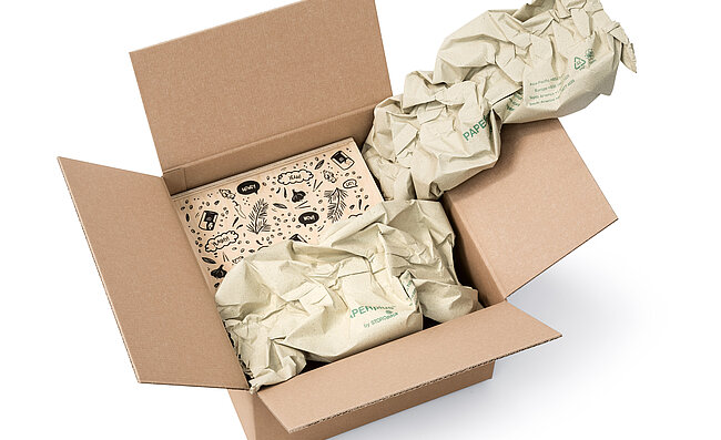 Una scatola di cartone contenente una scatola di legno e delle strisce d’imbottitura di carta prodotte con carta d’erba