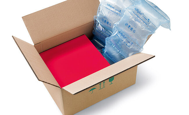 Una scatola di cartone contenente una scatola rossa e delle imbottiture d’aria 100% Recycled